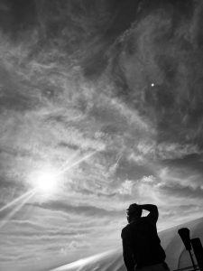 black and white photo of a person looking up at the sunny sky